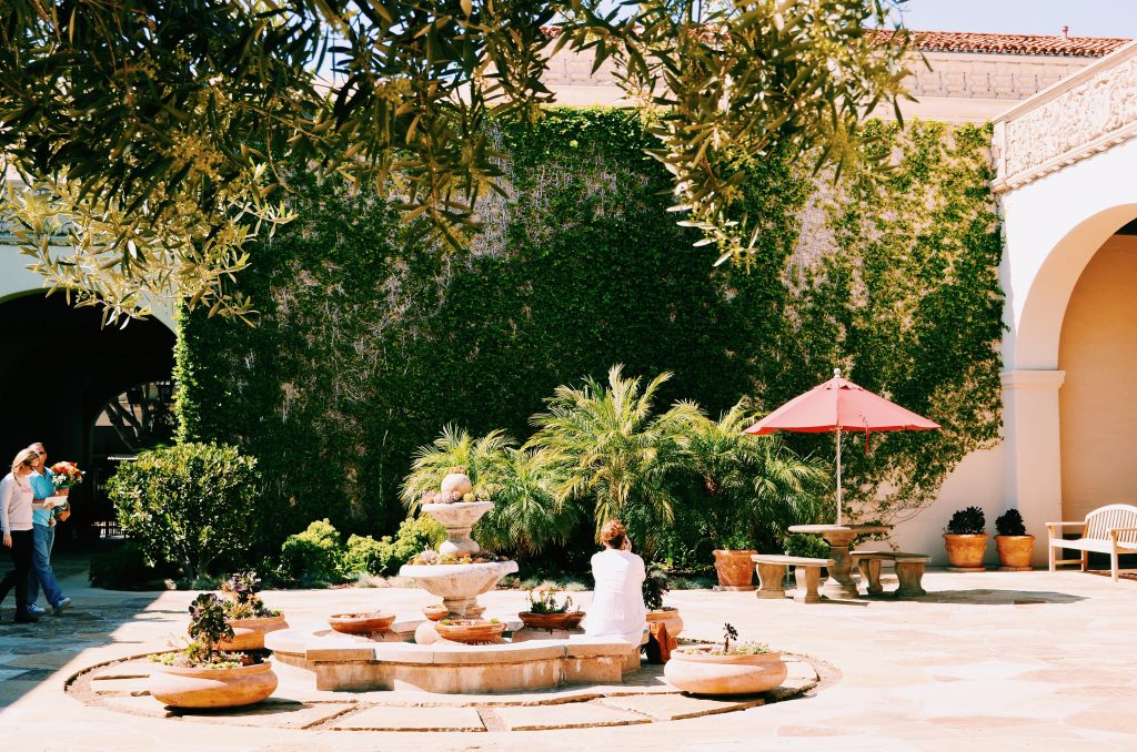 person sitting beside water foundation surrounded by trees